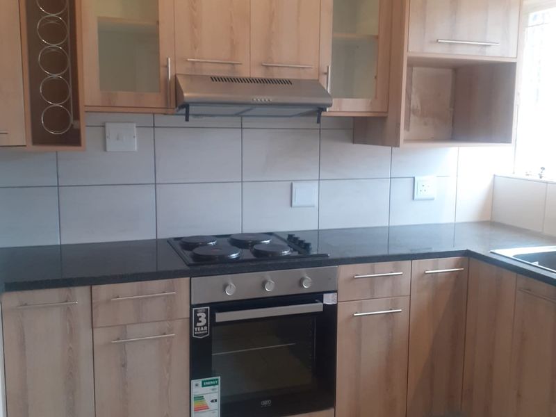 A clean, functional kitchen featuring light wood-finish cabinetry, granite countertops, a built-in oven, electric hob, and a tiled backsplash.