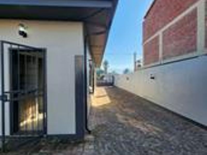A side exterior view of the property featuring cobblestone paving, a secure entrance gate, and a clean boundary wall.
