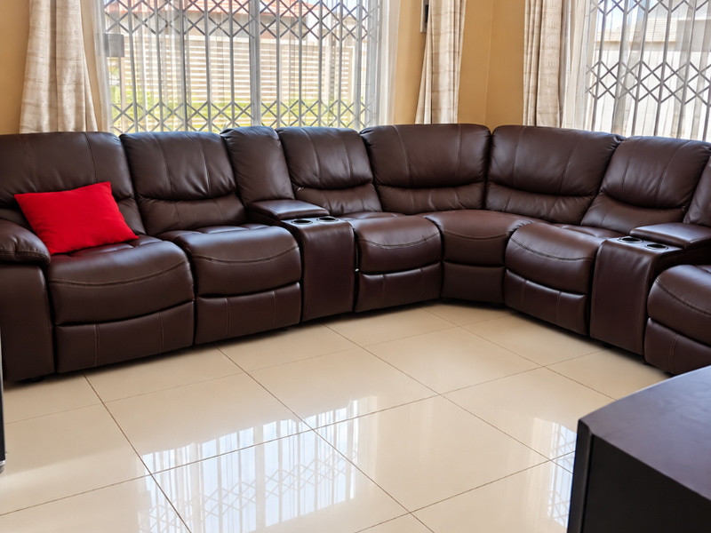 A bright living room featuring large windows with security gates, neutral porcelain floor tiles, and recessed ceiling lighting.