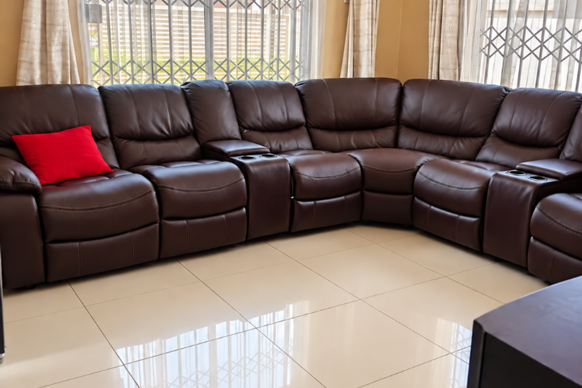 A bright living room featuring large windows with security gates, neutral porcelain floor tiles, and recessed ceiling lighting.
