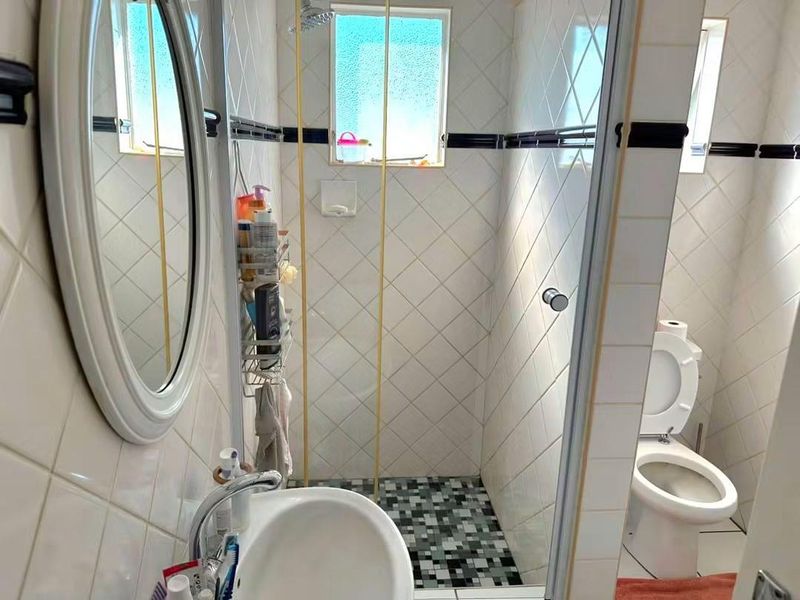 Compact bathroom featuring a shower enclosure, wall-mounted basin, and toilet with tiled finishes throughout.