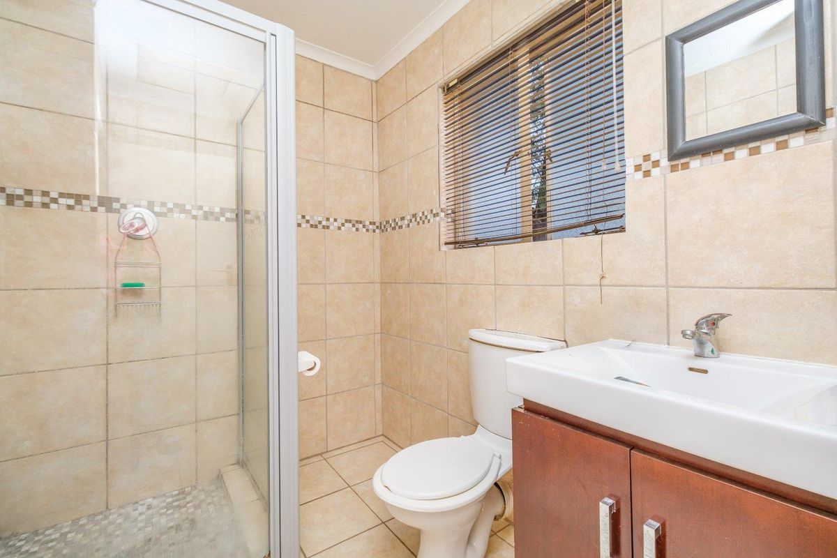 A functional bathroom featuring a shower enclosure, a vanity unit with a basin, and neutral wall and floor tiling.
