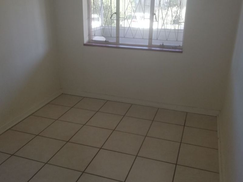 An empty bedroom featuring neutral tiled flooring and a window fitted with security bars.