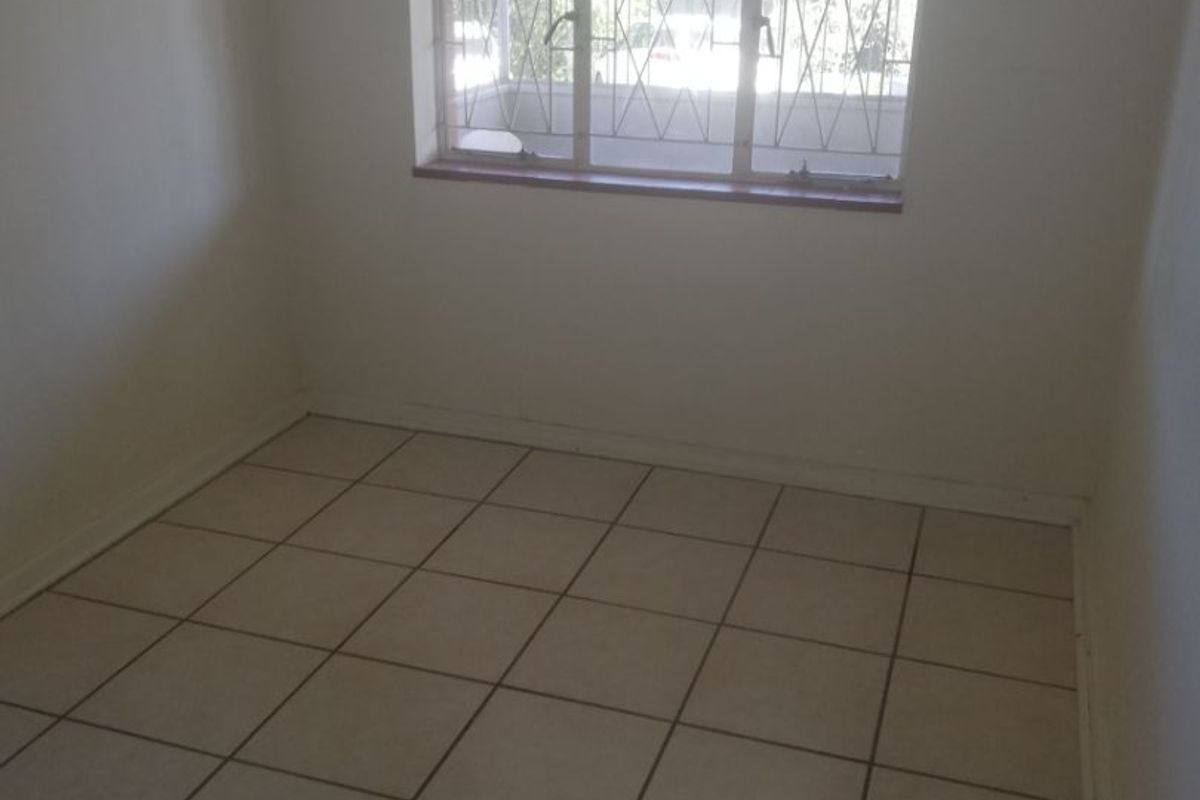 An empty bedroom featuring neutral tiled flooring and a window fitted with security bars.