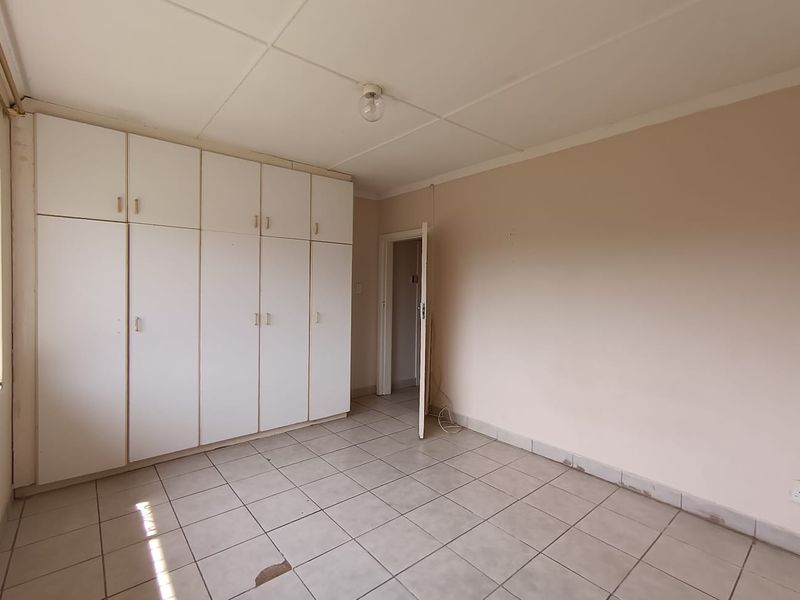 An empty bedroom featuring built-in white cupboards, tiled flooring, and a standard ceiling, offering a blank canvas for renovation or restyling.