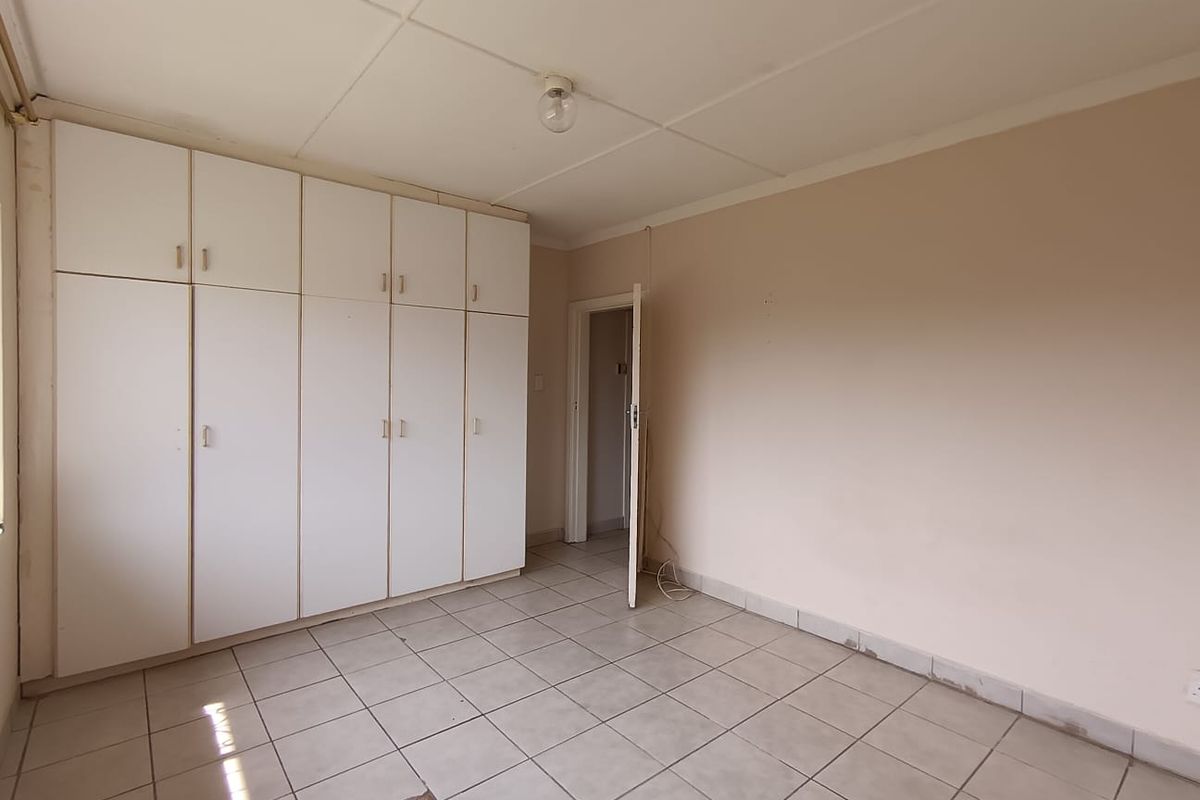 An empty bedroom featuring built-in white cupboards, tiled flooring, and a standard ceiling, offering a blank canvas for renovation or restyling.