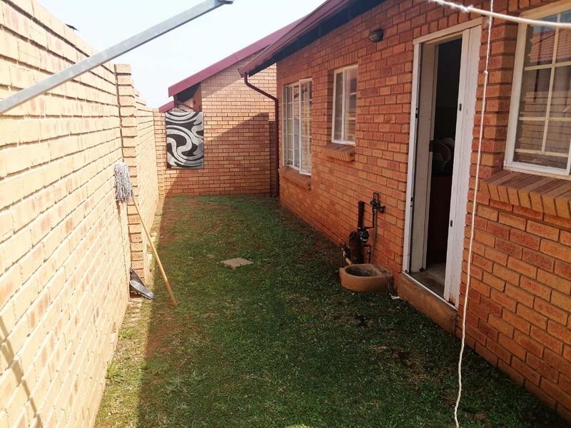 A side exterior view of the property featuring face brick walls, a small lawn area, and access to the interior via a door.