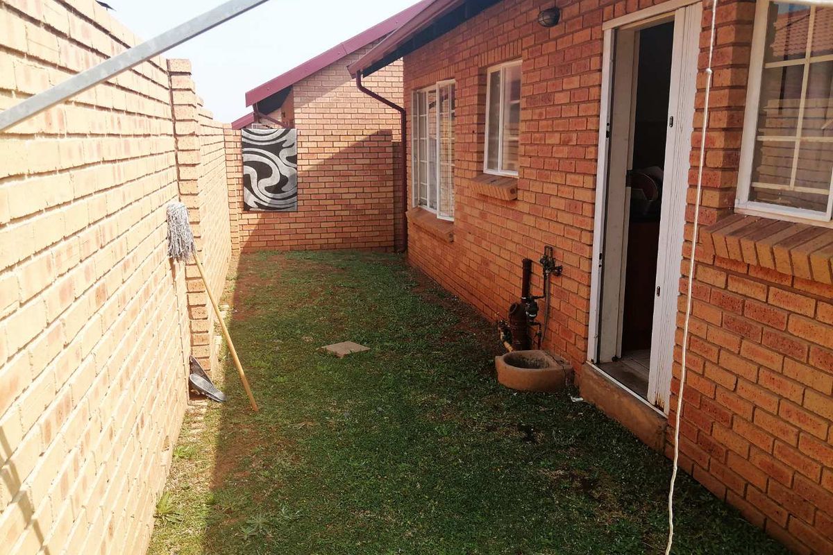 A side exterior view of the property featuring face brick walls, a small lawn area, and access to the interior via a door.