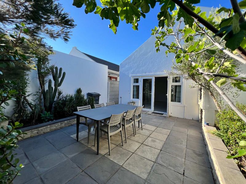 A private rear courtyard featuring a paved patio area, established garden beds, and direct access to the home through double glass doors.