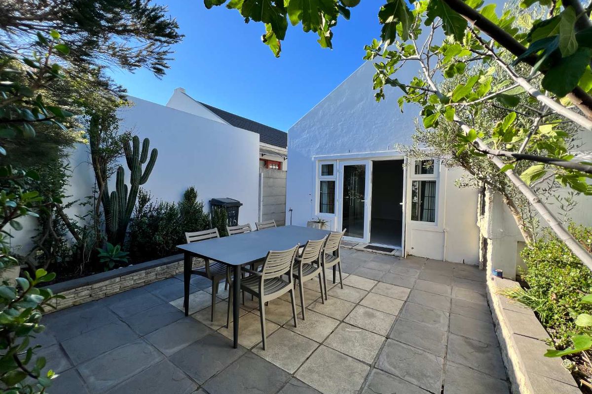 A private rear courtyard featuring a paved patio area, established garden beds, and direct access to the home through double glass doors.