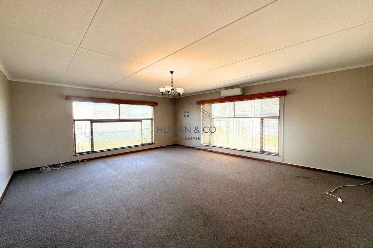 Spacious living room featuring large windows, wall-mounted air conditioning unit, and neutral carpeting.
