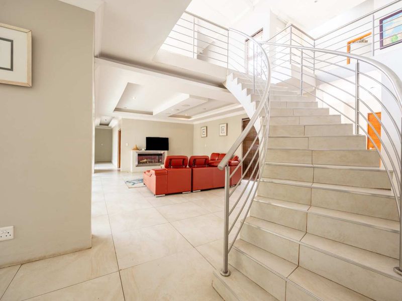 Spacious open-plan living area featuring a striking curved staircase with stainless steel balustrades, tiled flooring, and a modern built-in fireplace.