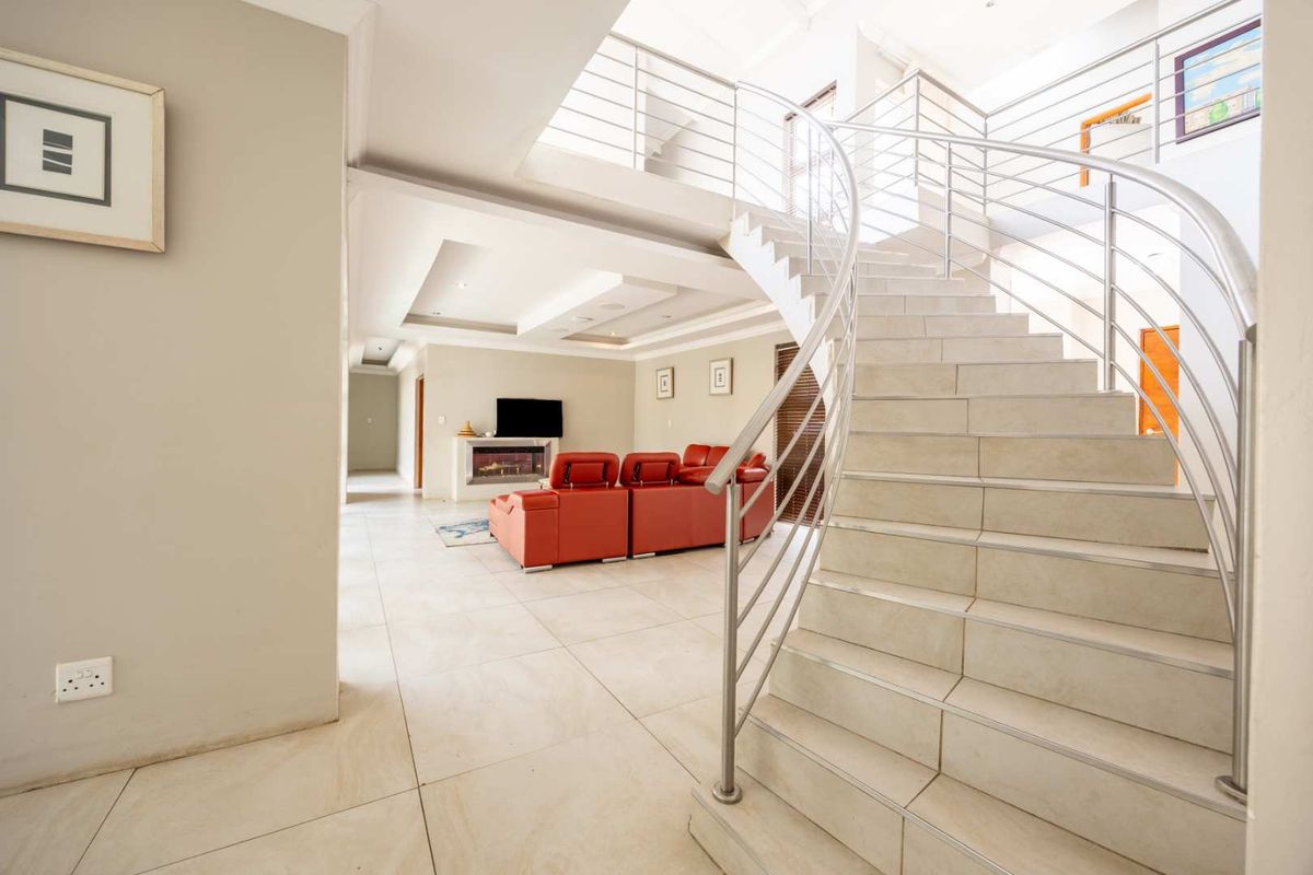 Spacious open-plan living area featuring a striking curved staircase with stainless steel balustrades, tiled flooring, and a modern built-in fireplace.