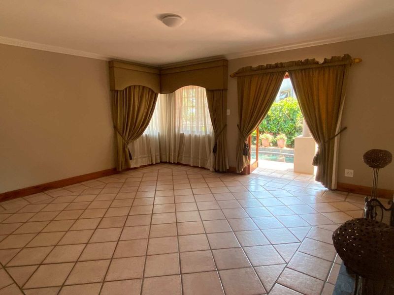 Spacious living room featuring ceramic tile flooring, cove molding, and direct access to the outdoor pool area through glass-paneled french doors.