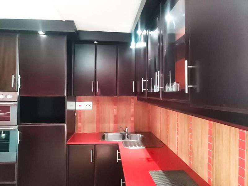 A functional kitchen featuring dark cabinetry, red laminate countertops, a double bowl stainless steel sink, and a built-in oven.