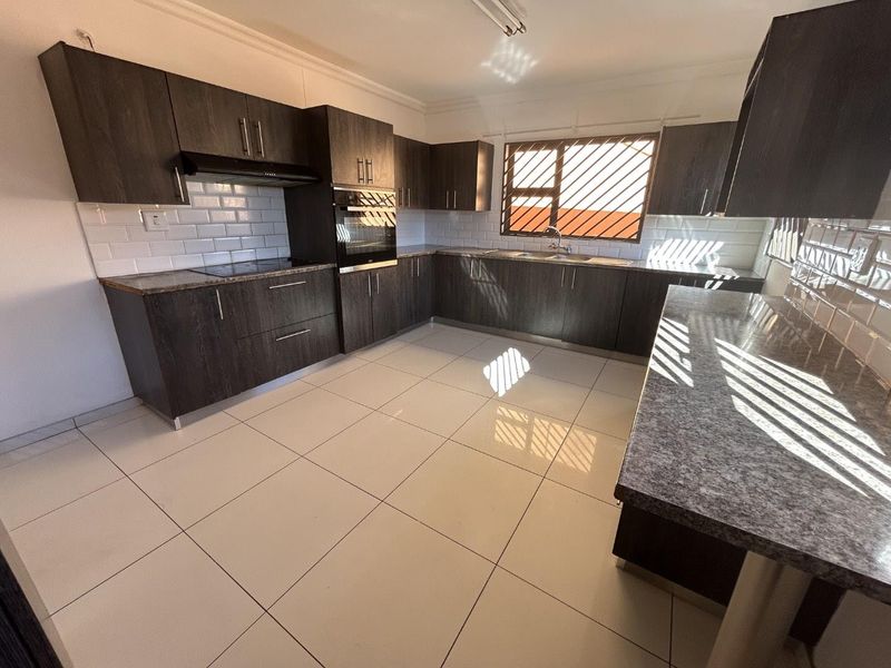 Modern kitchen featuring dark wood cabinetry, granite countertops, subway tile backsplash, built-in oven, and ceramic floor tiles.
