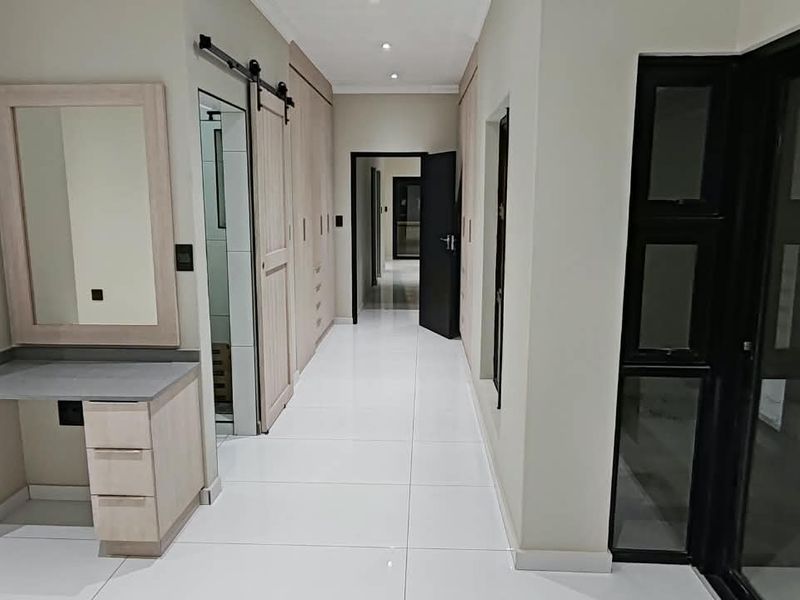 A modern, well-lit hallway featuring sleek tiled flooring, built-in cupboards, a vanity station, and a sliding barn door leading to an adjacent room.