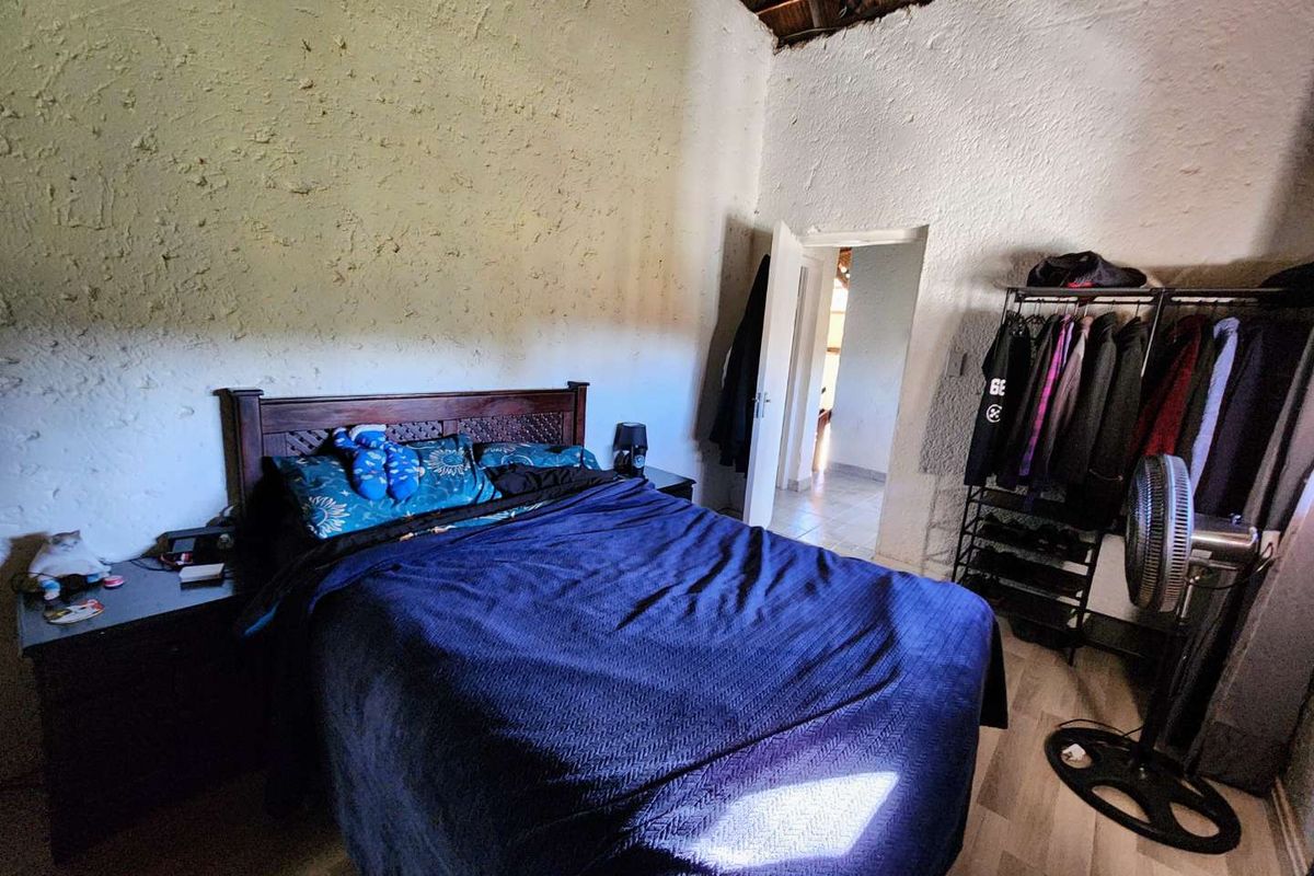A bedroom featuring a high-pitched exposed thatch ceiling and textured wall finishes, providing a rustic aesthetic with direct access to an adjoining room.
