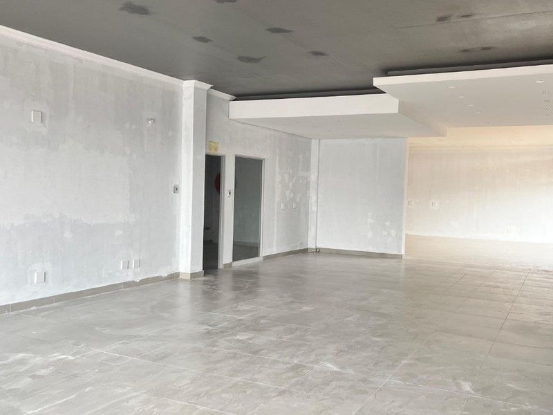 Spacious open-plan retail area featuring large format floor tiles and a modern dropped ceiling design, currently in an unfinished state awaiting final finishes.