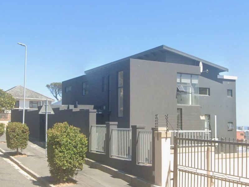 Modern multi-story cottage exterior featuring dark grey facade, secure metal gate, perimeter wall with electric fencing, and contemporary architectural design.