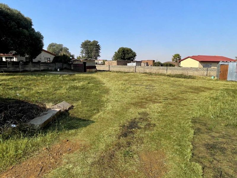A vacant residential plot featuring a perimeter wall and a small metal storage shed on the property.