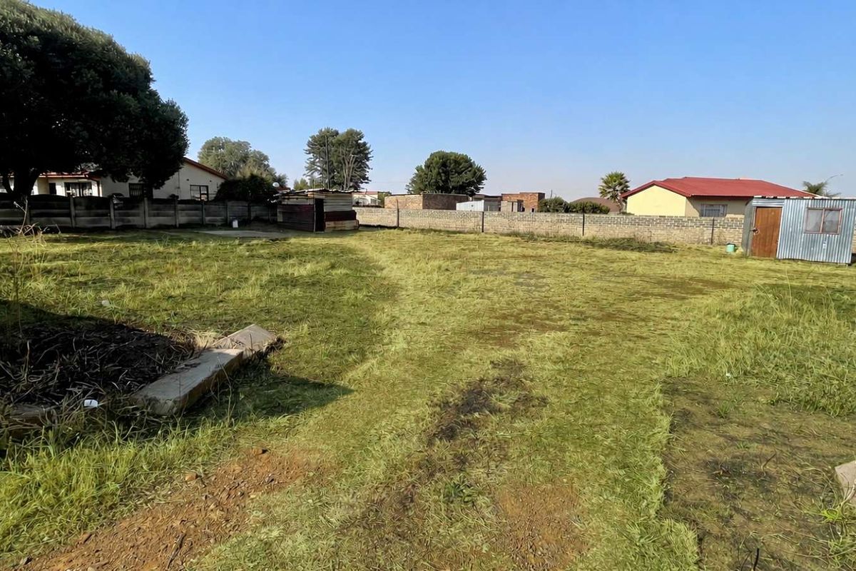 A vacant residential plot featuring a perimeter wall and a small metal storage shed on the property.