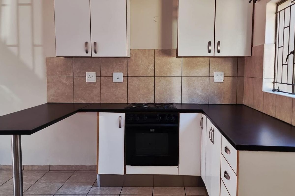 A functional kitchen featuring white cabinetry, dark countertops, a built-in oven with hob, and tiled splashbacks with a breakfast bar extension.