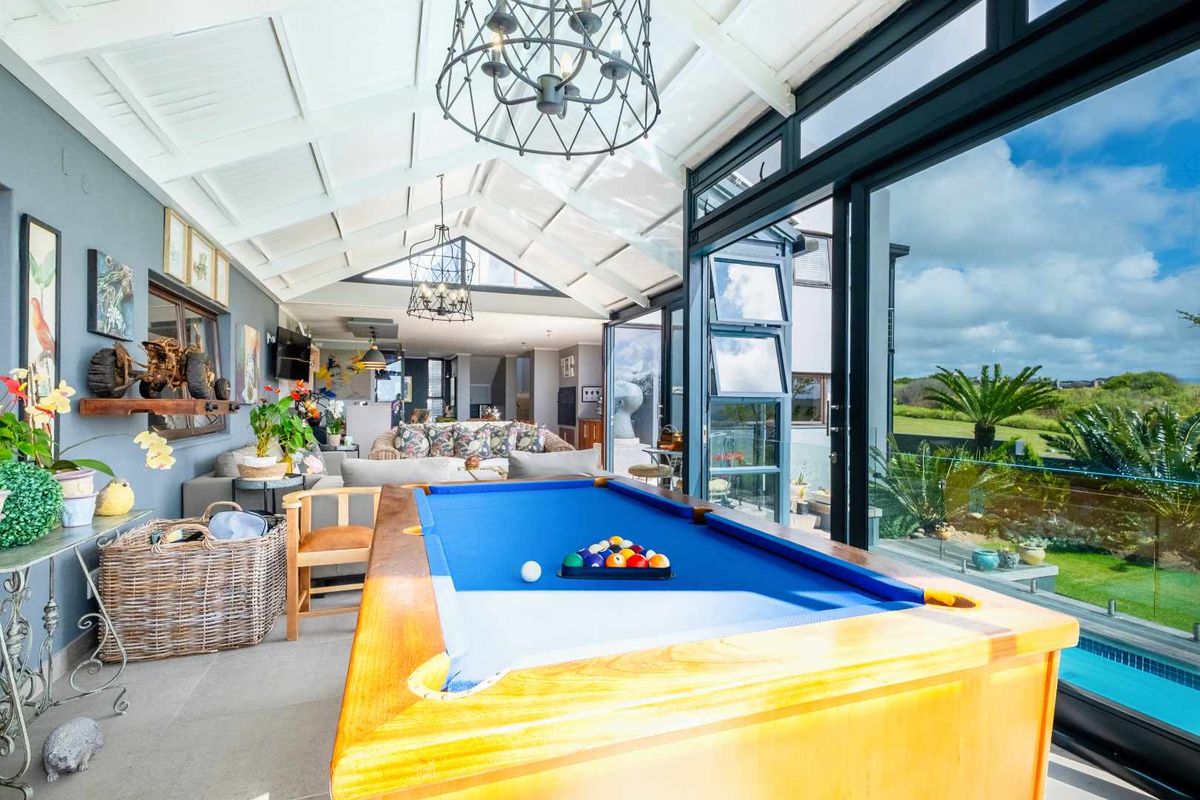 Spacious sunroom featuring a vaulted ceiling, exposed beams, and large glass sliding doors opening to a pool area and garden views.