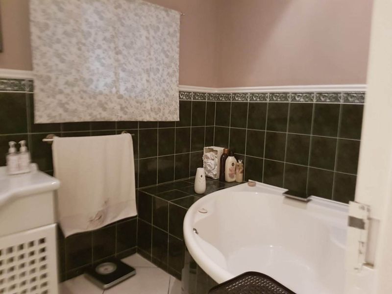 A bathroom featuring a built-in corner bathtub, tiled splashback with decorative border, and a vanity basin.