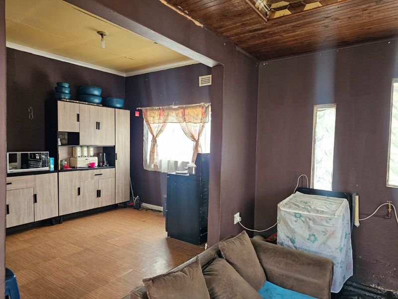 Open plan living and kitchen area featuring built-in cabinetry, timber ceiling paneling, and tiled flooring, requiring cosmetic updates to improve the overall aesthetic.