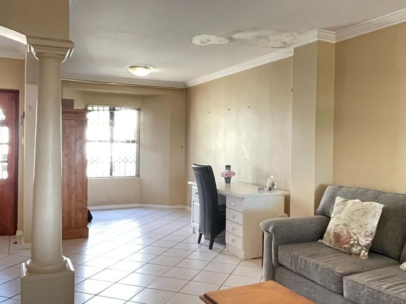 Spacious living area featuring tiled flooring, an architectural column, and an archway entrance. The ceiling shows visible signs of water damage.