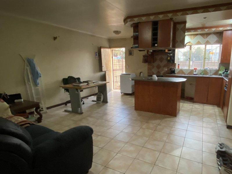 Open-plan living and kitchen area featuring tiled flooring, wooden cabinetry, and a central island, with direct access to an exterior security gate.