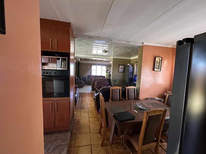 Open plan living and dining area featuring built-in kitchen appliances, tiled flooring, and a drop ceiling, requiring cosmetic updates to modernize the space.