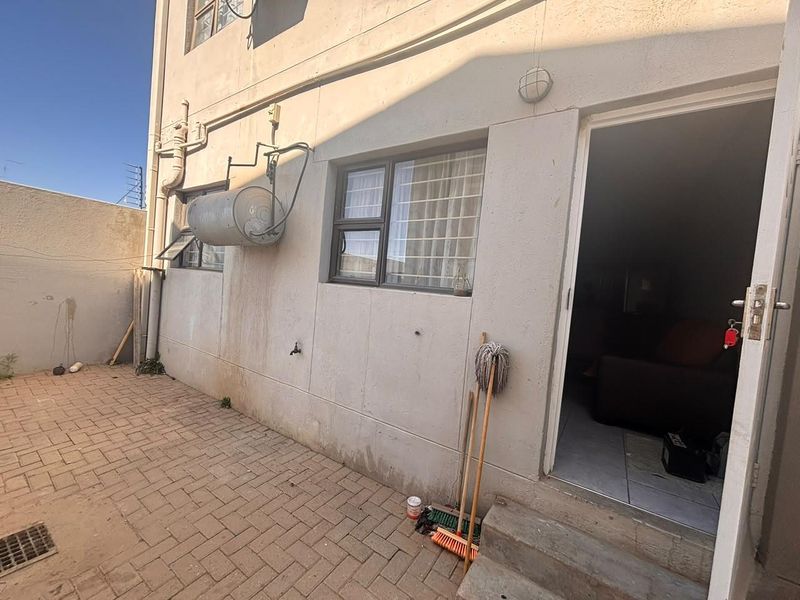 A rear courtyard area featuring paved flooring, an external geyser, and security bars on the windows, providing access to the apartment interior.
