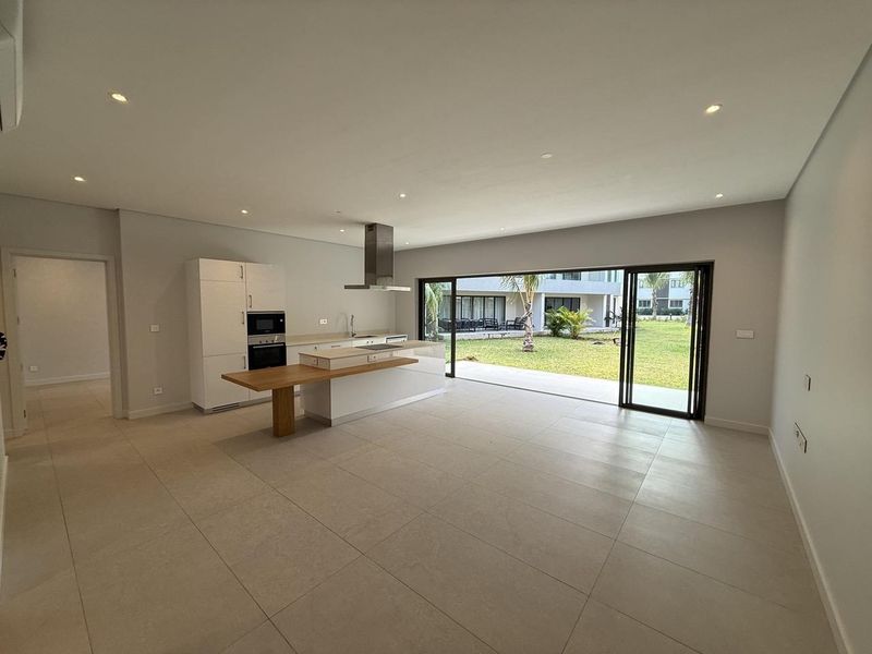 Spacious open-plan living and kitchen area featuring modern cabinetry, integrated appliances, and large sliding doors opening to a private garden.