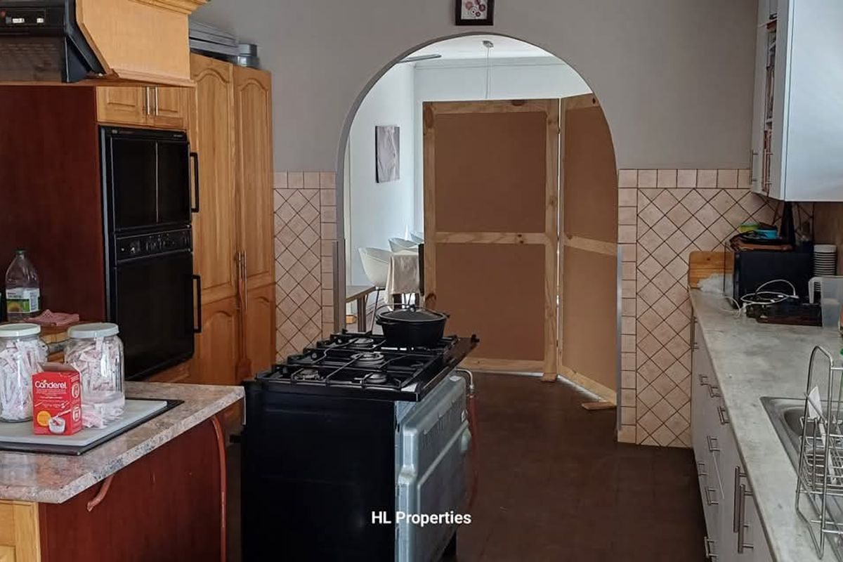 A functional kitchen featuring wooden cabinetry, a built-in oven, a gas stove, and a tiled backsplash, leading through an arched doorway.