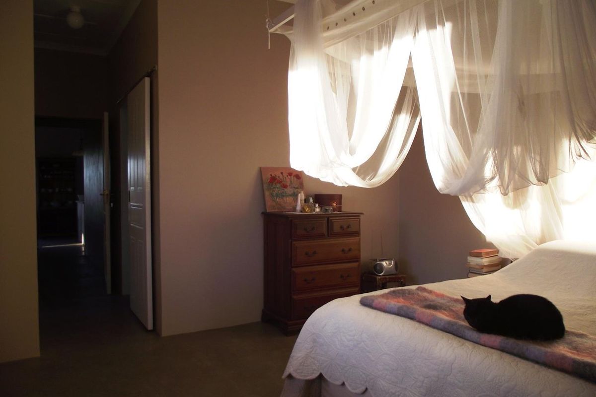 A bedroom featuring a four-poster bed frame with sheer curtains, neutral wall tones, and access to an adjacent hallway.