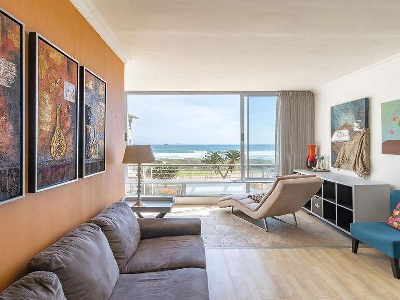 Bright living room featuring large sliding glass doors with ocean views, combining travertine and laminate flooring with a neutral interior finish.