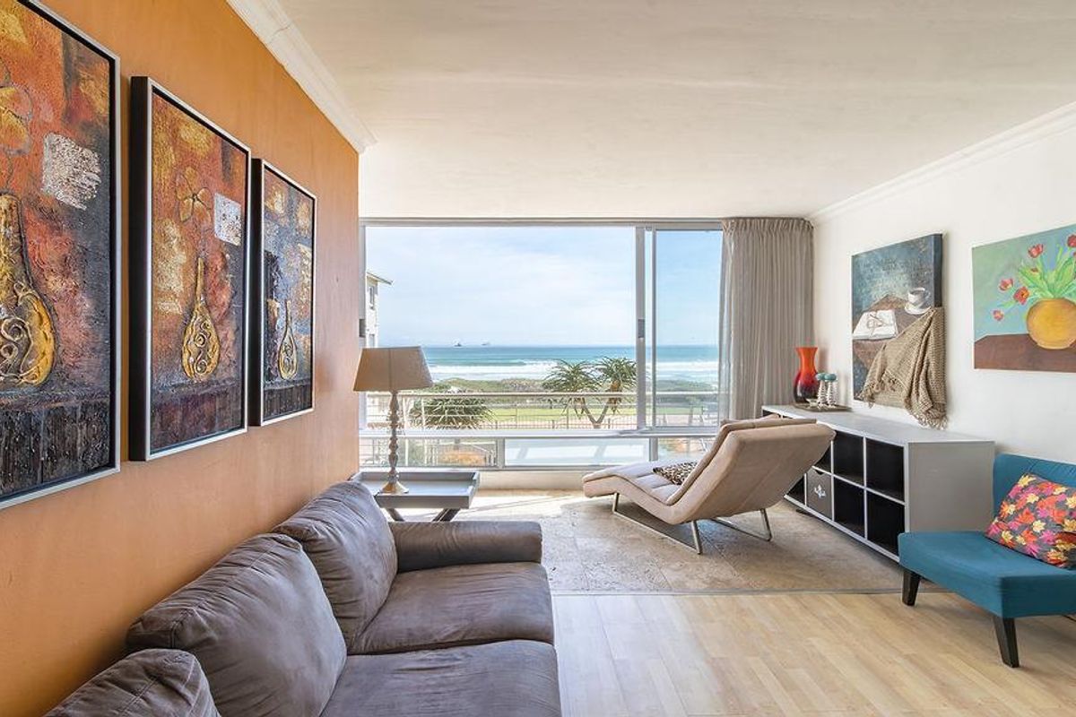 Bright living room featuring large sliding glass doors with ocean views, combining travertine and laminate flooring with a neutral interior finish.