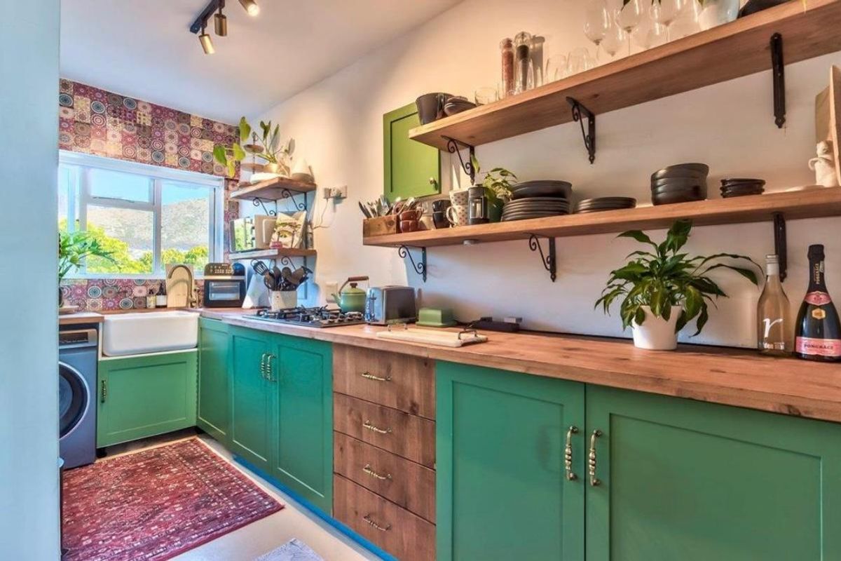 A charming kitchen featuring vibrant green cabinetry, natural wooden countertops, open shelving, and a classic farmhouse sink with a decorative tiled backsplash.