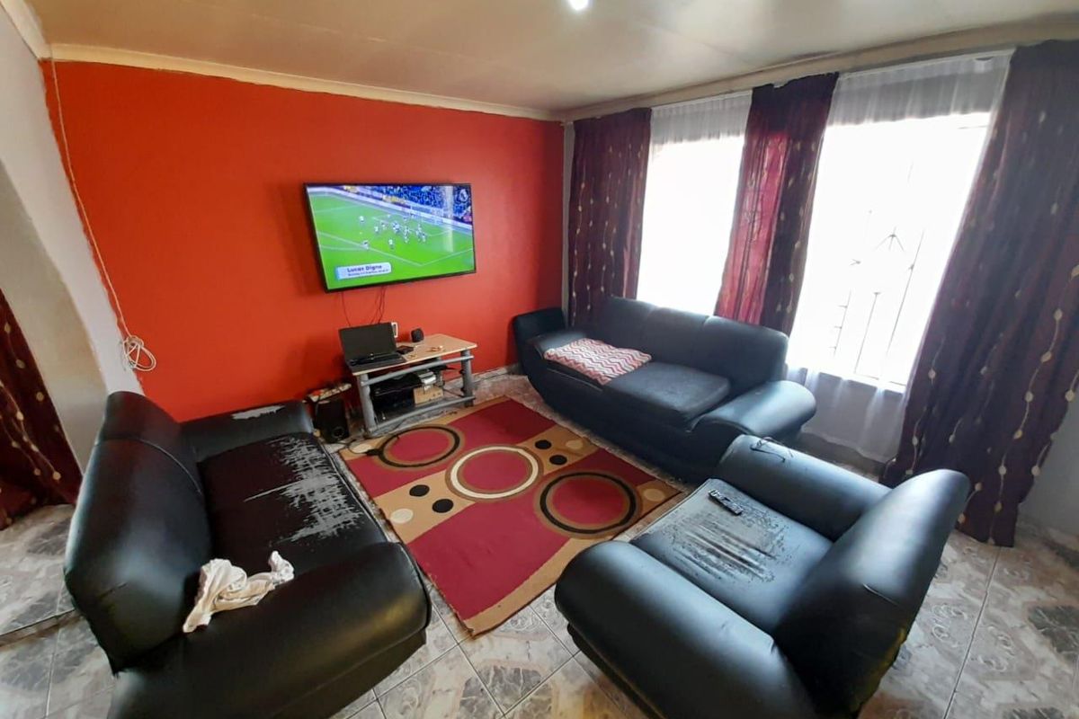 A living room featuring tiled flooring, a bold orange accent wall, and large windows with curtains.