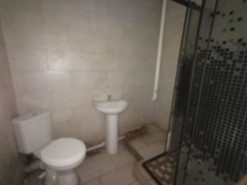 A functional bathroom featuring a pedestal basin, toilet, and shower enclosure with tiled finishes, requiring cosmetic updates to improve its overall condition.