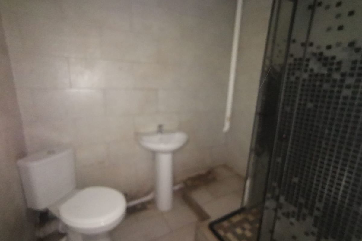 A functional bathroom featuring a pedestal basin, toilet, and shower enclosure with tiled finishes, requiring cosmetic updates to improve its overall condition.