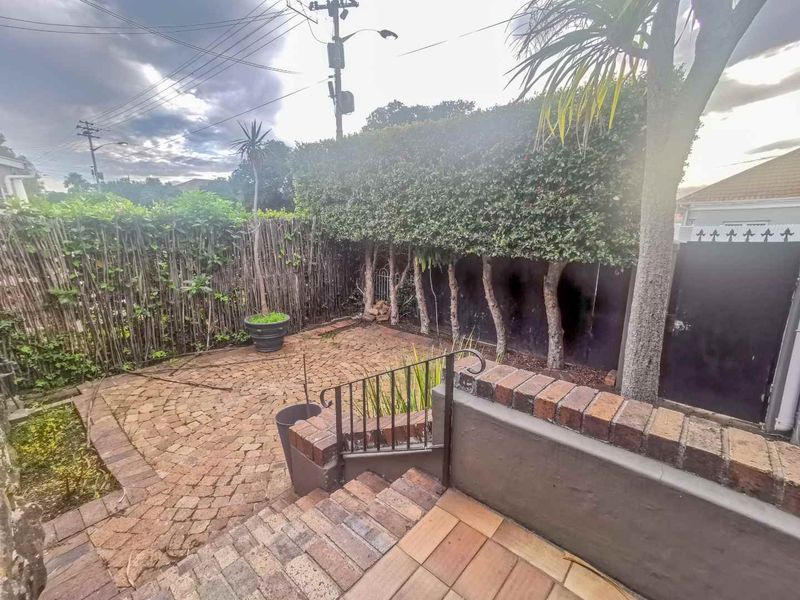 A private rear courtyard featuring brick paving, a retaining wall, and established hedge screening, providing a functional outdoor space.