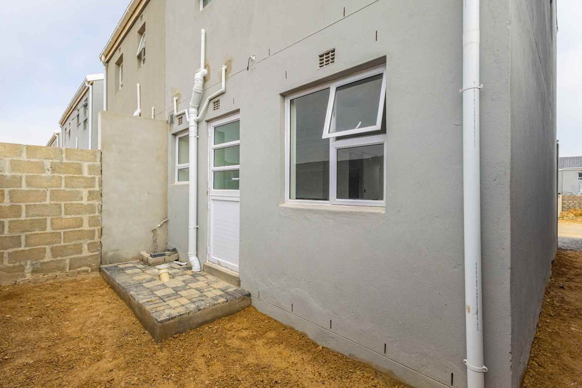 Rear exterior view of the townhouse featuring a paved patio area, exposed plumbing, and an unfinished garden space.