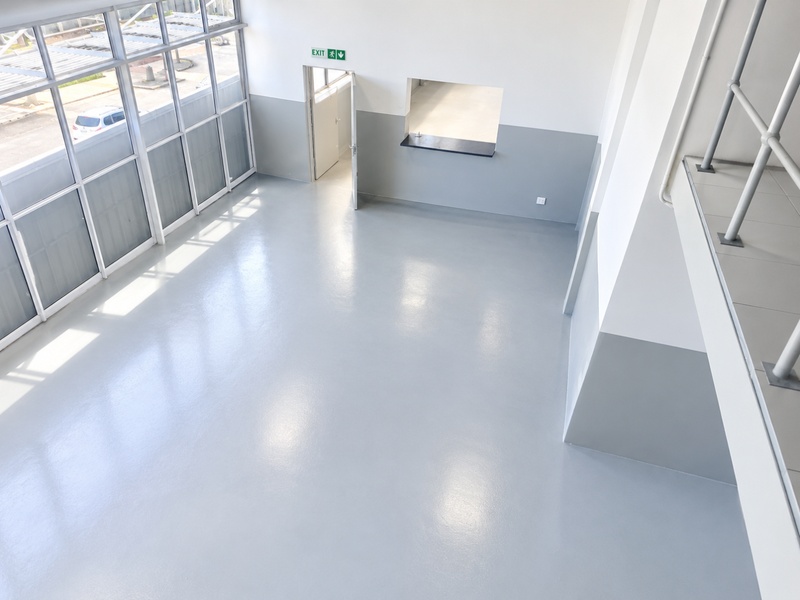 Spacious open-plan interior featuring polished epoxy flooring, large windows for natural light, a service hatch, and a mezzanine level with metal railings.