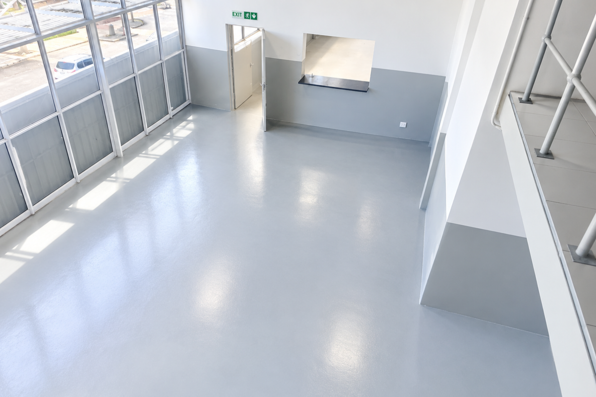 Spacious open-plan interior featuring polished epoxy flooring, large windows for natural light, a service hatch, and a mezzanine level with metal railings.