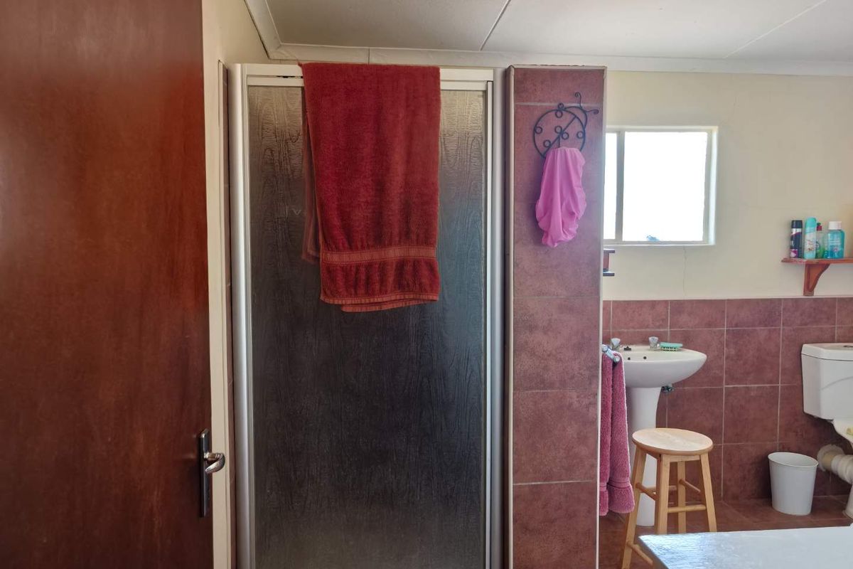 A functional bathroom featuring a shower enclosure, pedestal basin, and toilet with tiled splashbacks and natural light from a window.