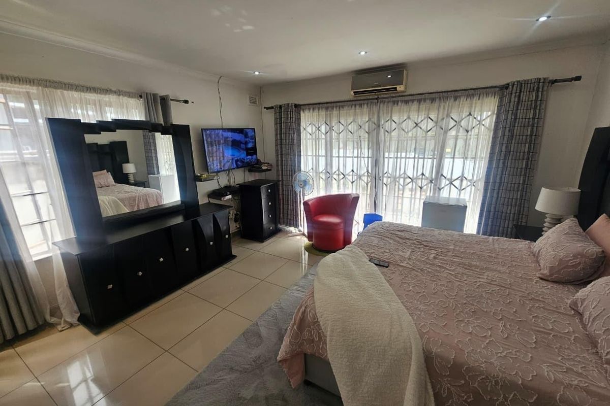 Spacious bedroom featuring tiled flooring, recessed downlighting, and a wall-mounted air conditioning unit, with direct access to an outdoor area via sliding glass doors.