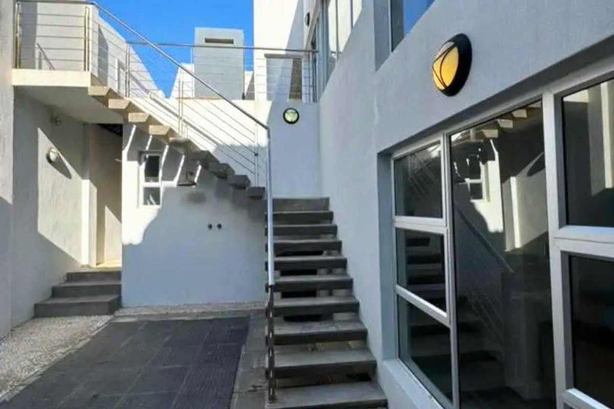 A modern exterior courtyard featuring concrete stairs, stainless steel railings, large glass windows, and paved flooring with decorative stone borders.